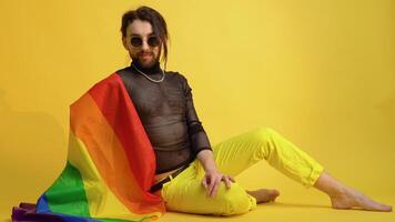 joven caucásico gay hombre 20s con arco iris a rayas bandera se sienta en amarillo antecedentes. personas estilo de vida Moda lgbtq concepto video