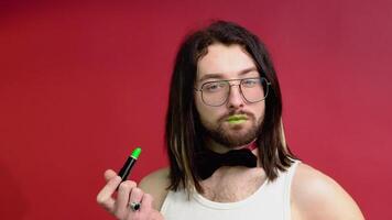 Young sexy gay man paints lips with green lipstick isolated on red background. People lifestyle fashion lgbtq concept video