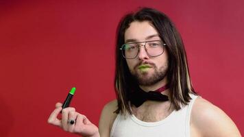 joven sexy gay hombre pinturas labios con verde lápiz labial aislado en rojo antecedentes. personas estilo de vida Moda lgbtq concepto video
