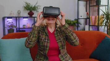 Senior woman using VR headset helmet app to play simulation game watching virtual reality home video