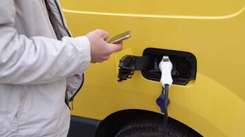 une homme utilisation intelligent téléphone tandis que attendre et Puissance la fourniture relier à électrique Véhicules pour mise en charge le batterie dans voiture video