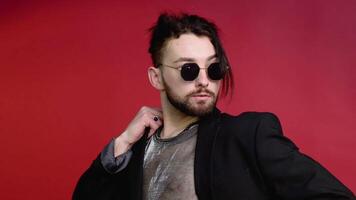 Portrait of a young gay man in sunglasses dressed in a mesh t-shirt on a red background video