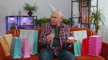 Happy senior elderly grandfather man celebrating birthday party, makes wish blowing burning candle video