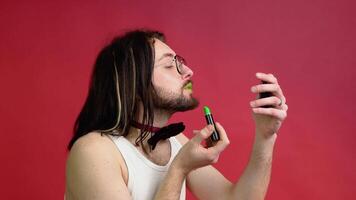 Young sexy gay man paints lips with green lipstick isolated on red background. People lifestyle fashion lgbtq concept video