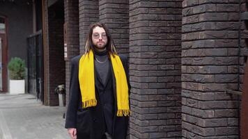 A young caucasian stylish man walks on the street in a coat with yellow scarf video