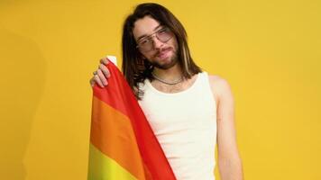 joven activista sonriente contento gay hombre sostener arco iris bandera aislado en amarillo antecedentes estudio. personas lgbt estilo de vida concepto video