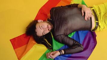 Young caucasian gay man with rainbow striped flag lies on yellow background. People lifestyle fashion lgbtq concept video