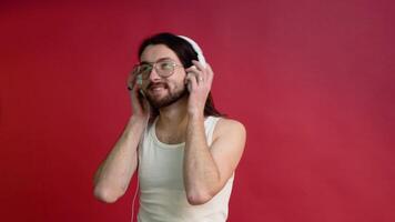 Jeune souriant content joyeux gay homme dans des lunettes et blanc T-shirt écoute à la musique sur rouge Couleur Contexte. mode de vie lgbtq fierté concept video