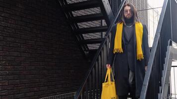 giovane caucasico elegante transessuale uomo al di fuori indossare cappotto e giallo sciarpa dopo shopping con giallo Borsa video