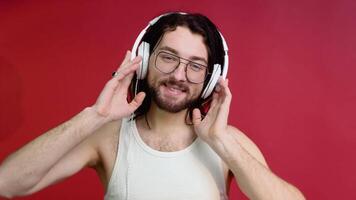 joven sonriente contento alegre metrosexual hombre en lentes y blanco camiseta escuchando a música en rojo color antecedentes video