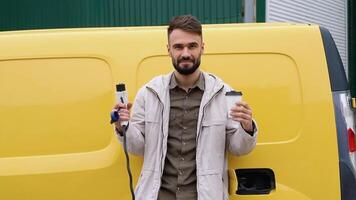 A man with a charger an coffee cup at a charging station looks into the camera video