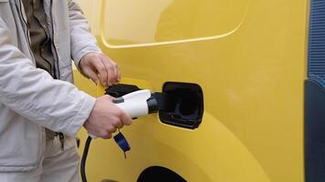 A man plugging in charging cable to electric vehicle and charges batteries. Male hand inserts power connector into cargo EV car video