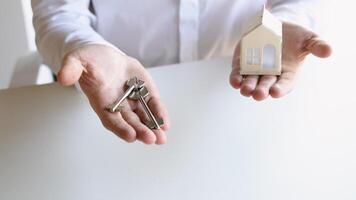 Close up view realtor broker holding home keys in his hand and white house model video