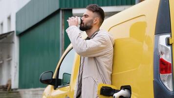 ein Mann Getränke Kaffee während Laden ein elektrisch Wagen. Grün Energie, Öko freundlich Treibstoff video