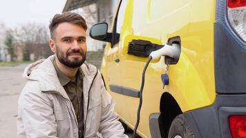 ung stilig skäggig turkiska man, plugging tråd in i de bil uttag till avgift hans frakt elektrisk bil på utomhus- laddning station i de stad video