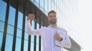 Smiling realtor standing outside modern house with key and documents video