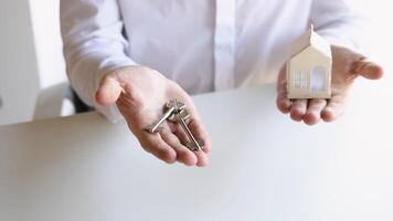 Close up view realtor broker holding home keys in his hand and white house model video