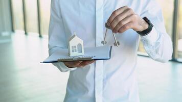 Close up view realtor broker holding home keys in his hand and white house model video