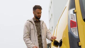 une homme débranche mise en charge câble électrique véhicule près entrepôt. vert énergie, éco amical carburant video