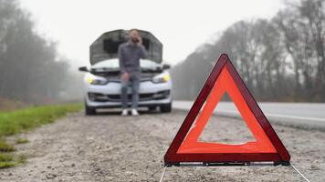 väg sida varning triangel, varning mötande trafik av en bruten ner bil, med en man använder sig av hans cell telefon till ring upp för bistånd. en man nära en bruten bil på en dimmig väg video