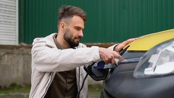 Stylish spanish man plugging in charging cable to electric vehicle and charges batteries. Male hand inserts power connector into cargo EV car video