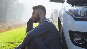 Young man sits near car talking on cell phone because his auto broken down. Turkish male trying to call friend that they help repair car video