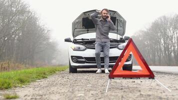 Frustrated spanish man stand front a broken car calling for assistance. A man near a broken car on a foggy road video