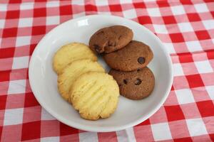 Chocolate chip cookies on a white plate with a checkered tablecloth top view photo