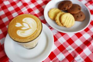 Choco chip cookies and latte coffee on a white plate with a checkered tablecloth seen above photo