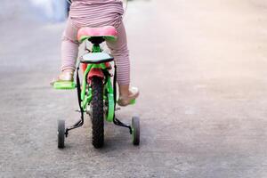 Child biker on the road, cycling adventure. Learning to ride a bike concept, Little girl is practicing cycling a bicycle with the training wheels on the road. photo