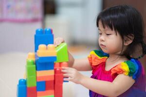 linda asiático niña es teniendo divertido jugando con vistoso el plastico bloques, un actividad ese mejora aprendiendo, disfrutando un divertido y educativo actividad, mano músculos y imaginación. niño Envejecido 3-4 años viejo. foto