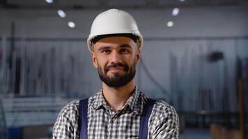 retrato do barbudo fábrica trabalhador dentro protetora capacete olhando às Câmera enquanto em pé dentro oficina video