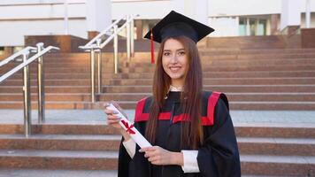 Young girl a student stands in a master's mantle and elegantly holds a diploma video