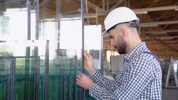 Professional man worker in uniform and helmet in a window warehouse prepares windows for sending video