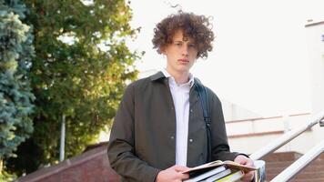 Young redhead curly student holds books posing with backpack near college building outdoor, smiling to camera. Modern education, college tuition and grants, studentship and study abroad concept video