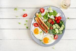 Keto breakfast. Fried eggs and chicken sausage and fresh salad. Top view, flat lay photo