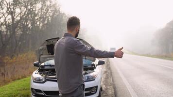 A man near a broken car on a foggy road stops passing transport video