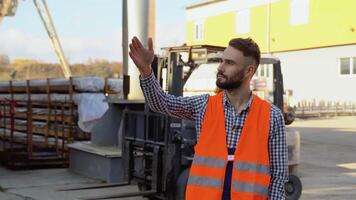 Serious manager in uniform giving commands to workers on industrial warehouse against the background of the warehouse loader. Bearded man gesturing and shouting during working process video