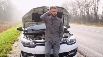 un sfortunato autista è nel shock vicino un' rotto auto nel il mezzo di il autostrada. un' rotto auto con un Aperto cappuccio su il lato di il nebbioso strada con il autista stringendo il suo testa video