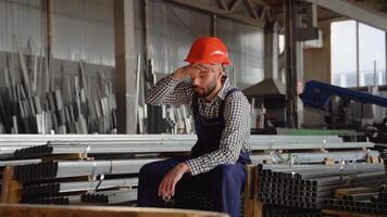 Tired worker in a helmet at a large metalworking plant. Professional worker in the warehouse of metal products video