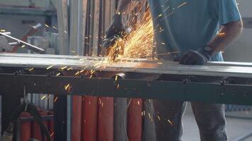 The interior of a heavy engineering plant with an industrial worker using an angular grinding machine and a cutting metal pipe video