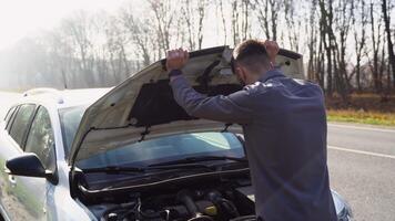 un sfortunato autista è nel shock vicino un' rotto auto nel il mezzo di il autostrada. un' rotto auto con un Aperto cappuccio su il lato di il strada con il autista stringendo il suo testa video