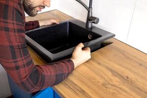 Man installing black stone sink into wooden countertop in kitchen. Close up photo