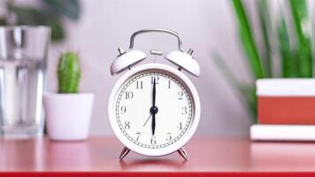 Classic white clock on a table. The clock hand points to at 6 close up photo