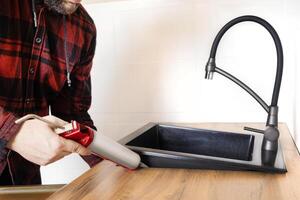 A man installs a black stone sink into a kitchen countertop. Worker seals up the kitchen sink with a sealant using a construction sealing gun photo