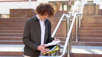 Young red -haired curly male student reads books near the university video