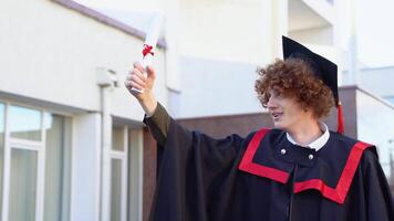 baixo ângulo retrato do feliz triunfante masculino graduado em pé perto universidade segurando acima diploma video