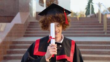 Funny red -haired graduate corrects the hairstyle with a diploma. Curly graduate with braces smiles near the college video