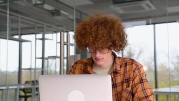 fatigué déçu programmeur séance à une table dans Bureau et travail sur une ordinateur portable, porte Jaune chemise. Jeune blogueur crée Nouveau contenu pour le sien Blog, jouit le travail de une pigiste video