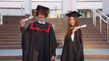 el chico y niña graduados de el magistratura son fácil y alegremente en pie en el rayos de el Dom con diplomas en su manos video